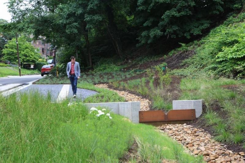 Man walks beside a channel of river rock running between two concrete borders.
